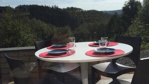 Ein Essbereich im Freien mit einem runden Tisch und Stühlen vor einer bewaldeten Landschaft.