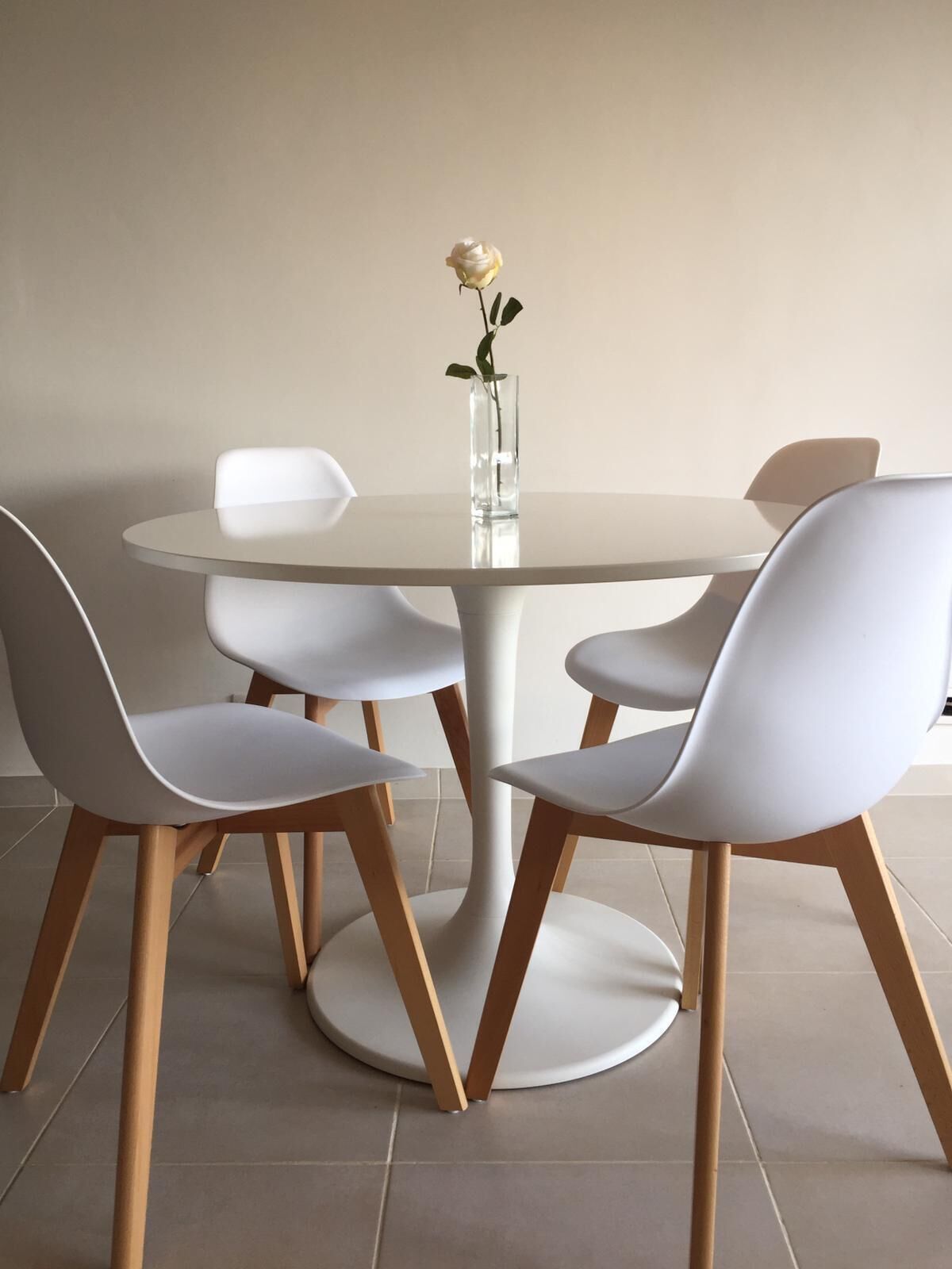 A round table with four white chairs and a vase with a single white rose.
