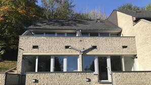 Ein zweistöckiges Haus mit Naturstein-Fassade, großen Fenstern und einer flachen Dachfläche.