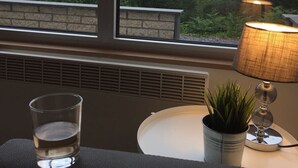 Ein Zimmer mit Blick auf einen bewaldeten Hügel, ein Fenster mit Aussicht, eine Lampe, ein Glas Wasser und ein Blumentopf.