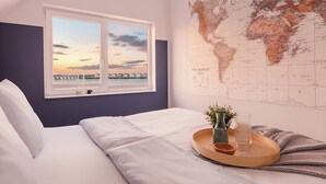 A bedroom with a large window, a world map on the wall, and a wooden tray with a vase and glass on the bed. - Baltic Sea vacation in the "Hafenkieker": Fantastic vacation apartment with sauna and sea view! (Olpenitz)