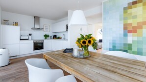 A modern kitchen with white cabinets, a wooden dining table, and a wall with a color palette. - Baltic Sea vacation in the "Hafenkieker": Fantastic vacation apartment with sauna and sea view! (Olpenitz)
