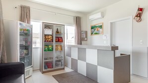 Un moderno vestíbulo de hotel con un mostrador de recepción a cuadros, un refrigerador con bebidas y una zona de estar con sofá, además de vistas al exterior.