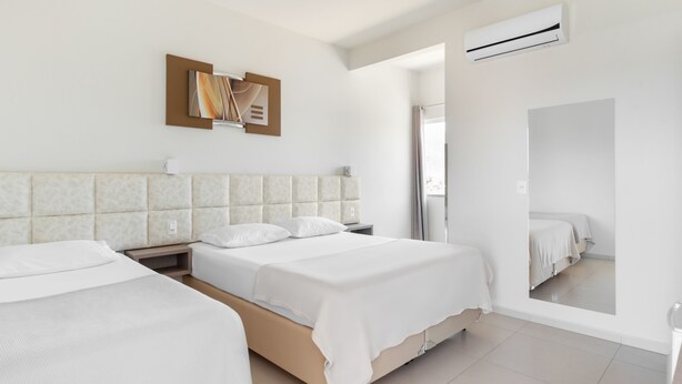 Una habitación de hotel moderna con dos camas, un espejo grande, un equipo de aire acondicionado y vistas al exterior.