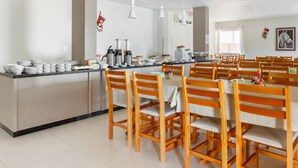 Un amplio comedor con sillas y mesas de madera, un mostrador de buffet con diversas opciones de comida y un diseño moderno en el techo.