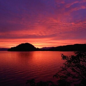 Atardecer sobre un lago tranquilo, con la silueta de una colina al fondo.