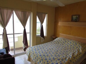 Habitación de hotel con cama, ventana con cortinas, una mesita y un cuadro en la pared.
