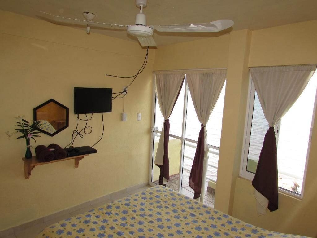 A bedroom with a bed, a ceiling fan, a TV mounted on the wall, and a window with curtains.