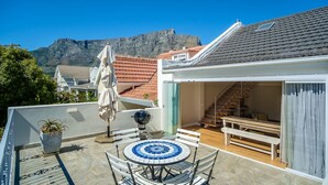 A rooftop terrace with a round table, a barbecue grill, and a view of a mountain. - Sublime Cottage near Table Mountain and Kloof Street (Tamboerskloof)