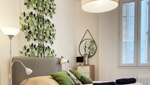 Une chambre à coucher comprenant un lit, une table de chevet, une lampe, un miroir et un mur orné d’un motif végétal.