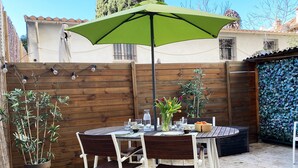 Une table en bois avec des chaises, un parasol vert et une plante en pot, le tout installé dans un espace extérieur aménagé.