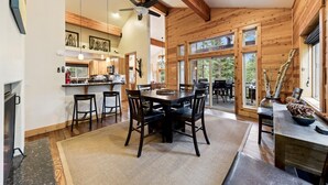 A spacious kitchen with wooden cabinets, a dining area with a large table and chairs, and a view of the outdoors through large windows. - Blue Moose -2 Masters, Hot Tub + Generator (Truckee)