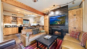 A cozy living room with a fireplace, a sofa, a coffee table, and a TV mounted on the wall. - Blue Moose -2 Masters, Hot Tub + Generator (Truckee)