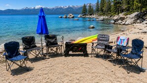 A lakeside view with clear skies, a row of camping chairs, a blue umbrella, and a bag of camping gear. - Blue Moose -2 Masters, Hot Tub + Generator (Truckee)