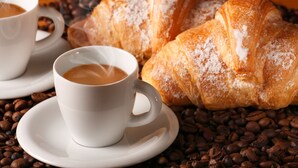 A cup of coffee with steam, a pastry, and coffee beans. - Rubino Guest House (Rome)