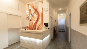 A reception area with a modern design, featuring a reception desk, a clock, and a fire extinguisher. - Rubino Guest House (Rome)