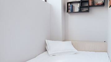 A minimalist bedroom with a bed, a window, and a wall-mounted bookshelf.