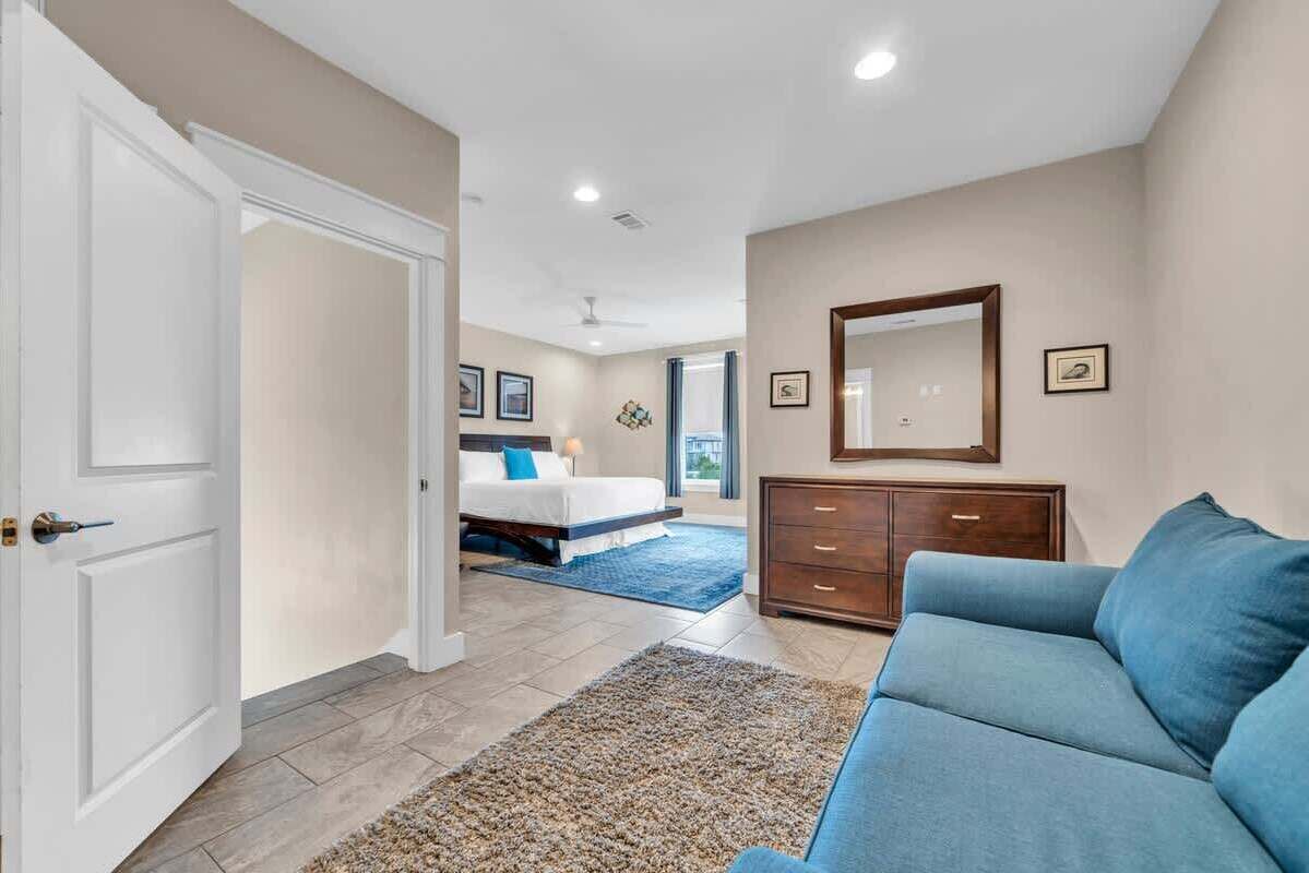 A bedroom with a bed, a dresser, a blue sofa, and a large mirror on the wall.