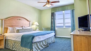 A hotel room with a bed, a desk, a television, a window with curtains, and a ceiling fan. - Good Times and Tan Lines! (Daytona Beach)