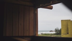 A wooden cabin with a view of the ocean through a window. - Pousada Pé na Areia (Garopaba)