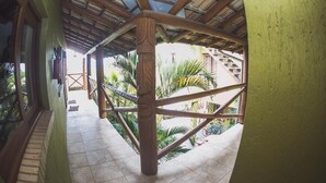 A covered outdoor area with a wooden structure, tiled floor, and a view of a garden with palm trees. - Pousada Pé na Areia (Garopaba)