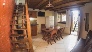A rustic kitchen with wooden cabinets, a dining table with chairs, and a staircase. - Pousada Pé na Areia (Garopaba)