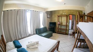A room with a bed, a sofa, a television, and a dog. - Pousada Pé na Areia (Garopaba)