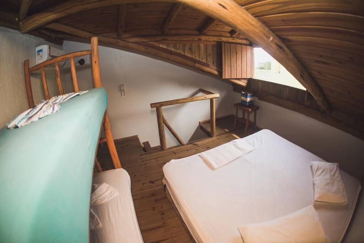 A small, rustic room with a sloped ceiling, wooden walls, and a simple bed.