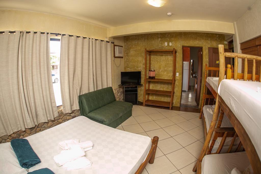 A hotel room with a bed, a green sofa, a TV, and a wooden bunk bed.