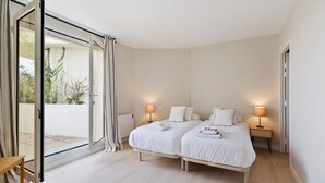 Un dormitorio con dos camas, una puerta corrediza de vidrio a un balcón y lámparas de noche.