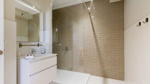Un baño moderno con ducha de vidrio, tocador blanco con espejo y pared con azulejos.