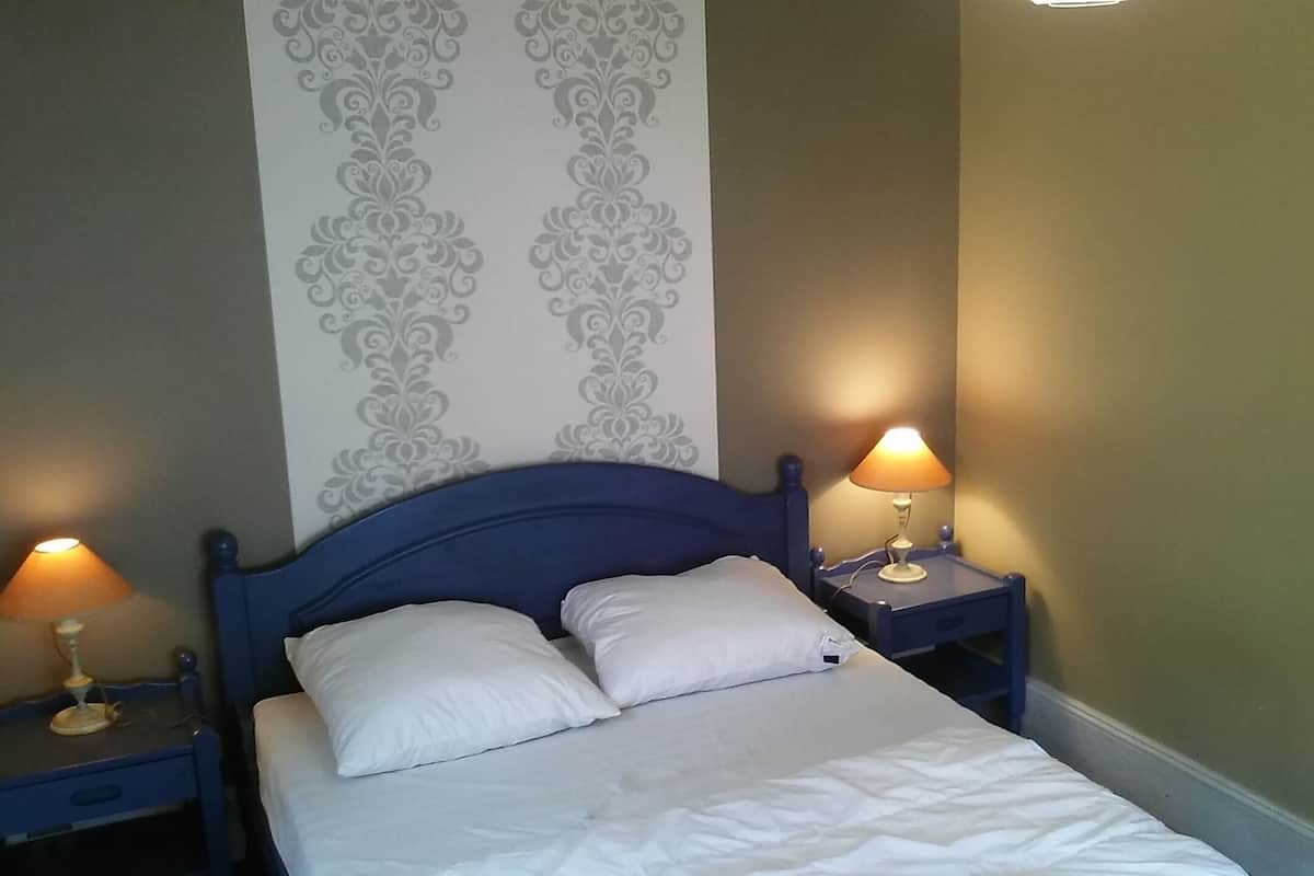 Una cama bien hecha con dos almohadas, flanqueada por dos mesitas de noche con lámparas, frente a una pared con un diseño decorativo.