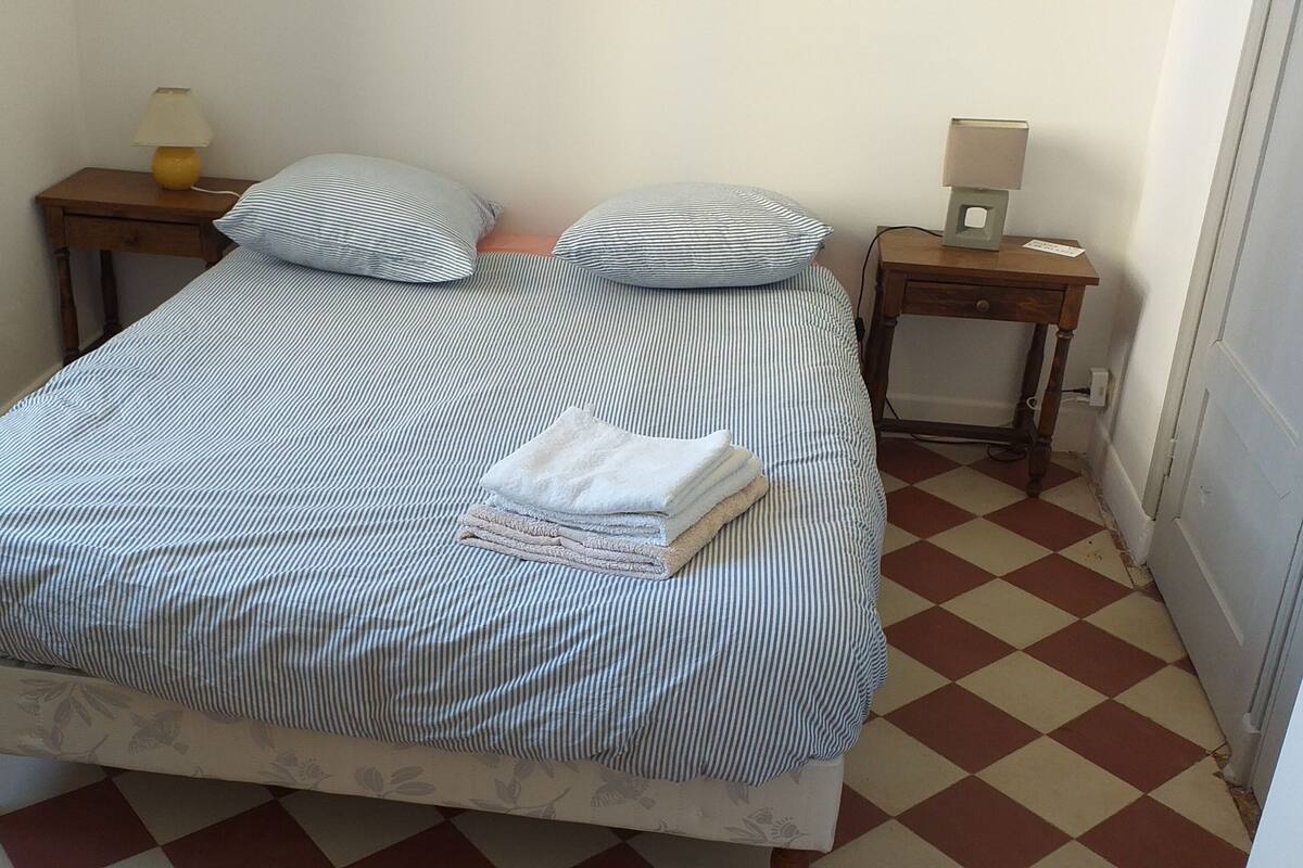Una cama con ropa de cama a rayas, dos mesitas de noche con lámparas y un suelo de cuadros.