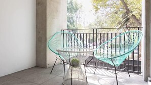 Un balcone con due sedie in filo di ferro color turchese e un tavolo bianco, con vista su alberi e una strada.