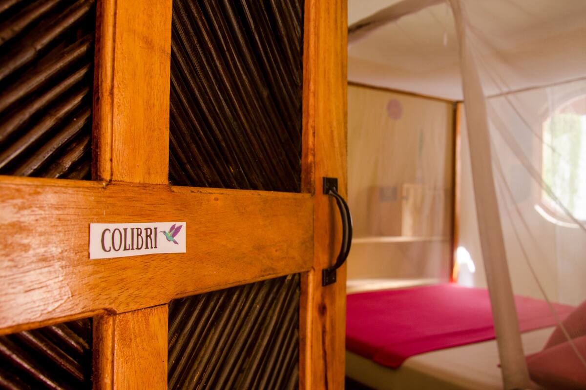 Una puerta de madera con un letrero que dice "COLIBRI" y una mosquitera al fondo.