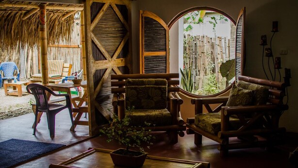 Una habitación rústica con muebles de madera, un ventanal con vistas a la vegetación y una estructura de techo de paja.