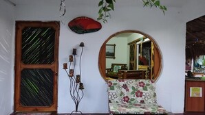 Una habitación con puerta de madera, espejo redondo, sofá floral y un atrapasueños colgado en la pared.