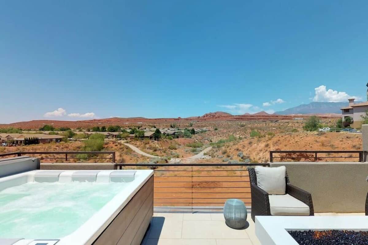 A rooftop terrace with a hot tub, seating area, and a view of a desert landscape.