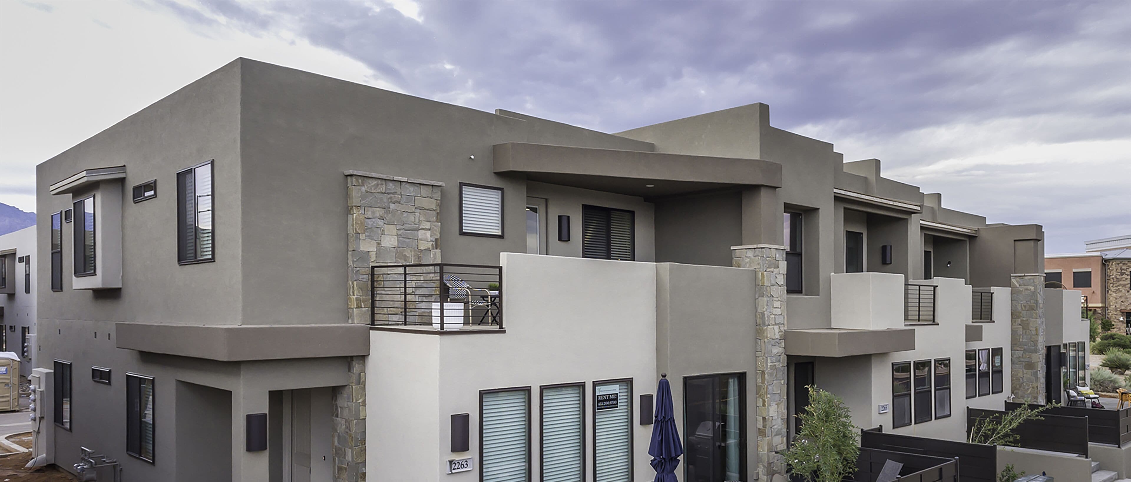 A modern multi-story residential building with a stone accent wall, balconies, and a clear view of the surrounding area.