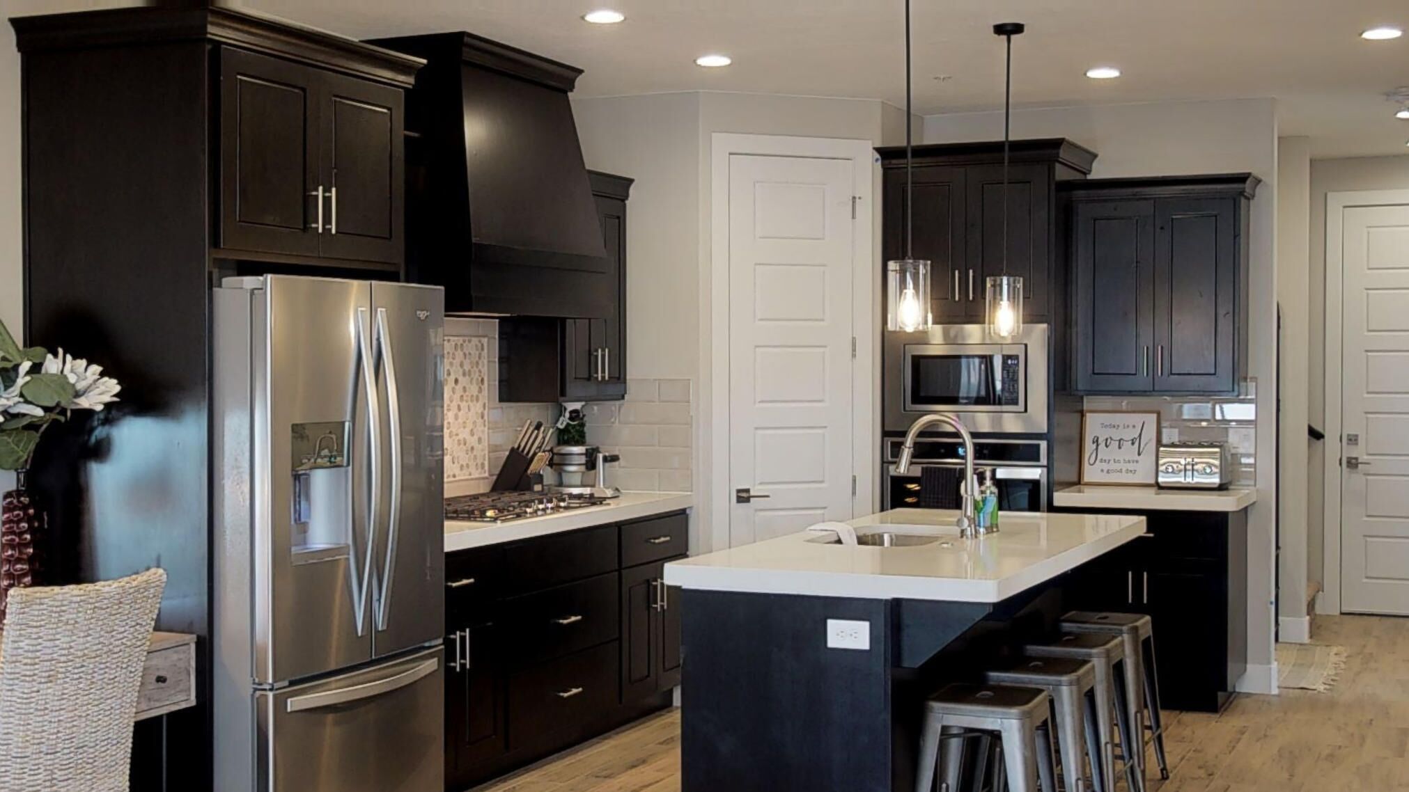 A modern kitchen with dark cabinetry, stainless steel appliances, and a central island with stools.
