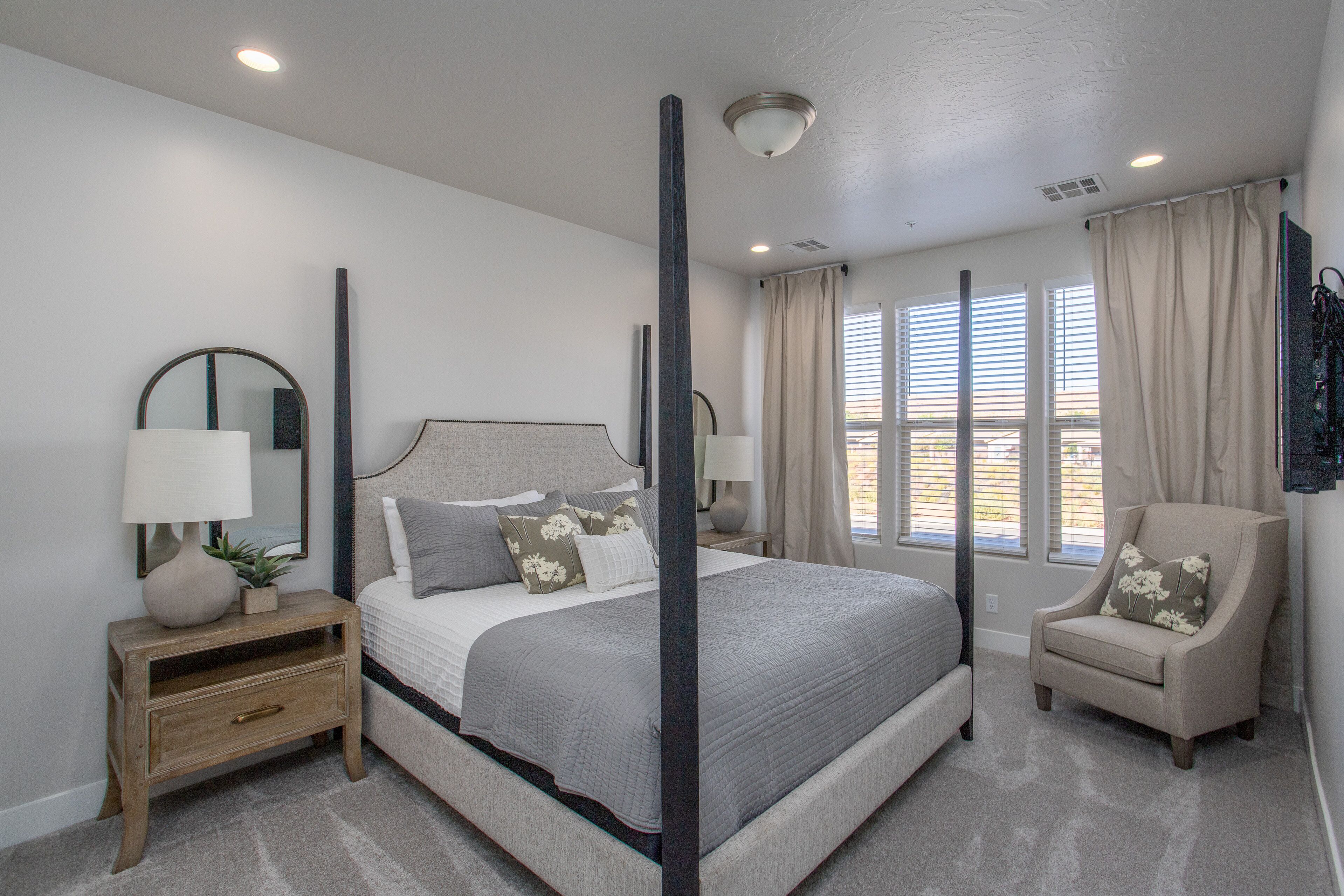 Quarto com cama de dossel, mesa de cabeceira, cadeira e uma grande janela com cortinas.