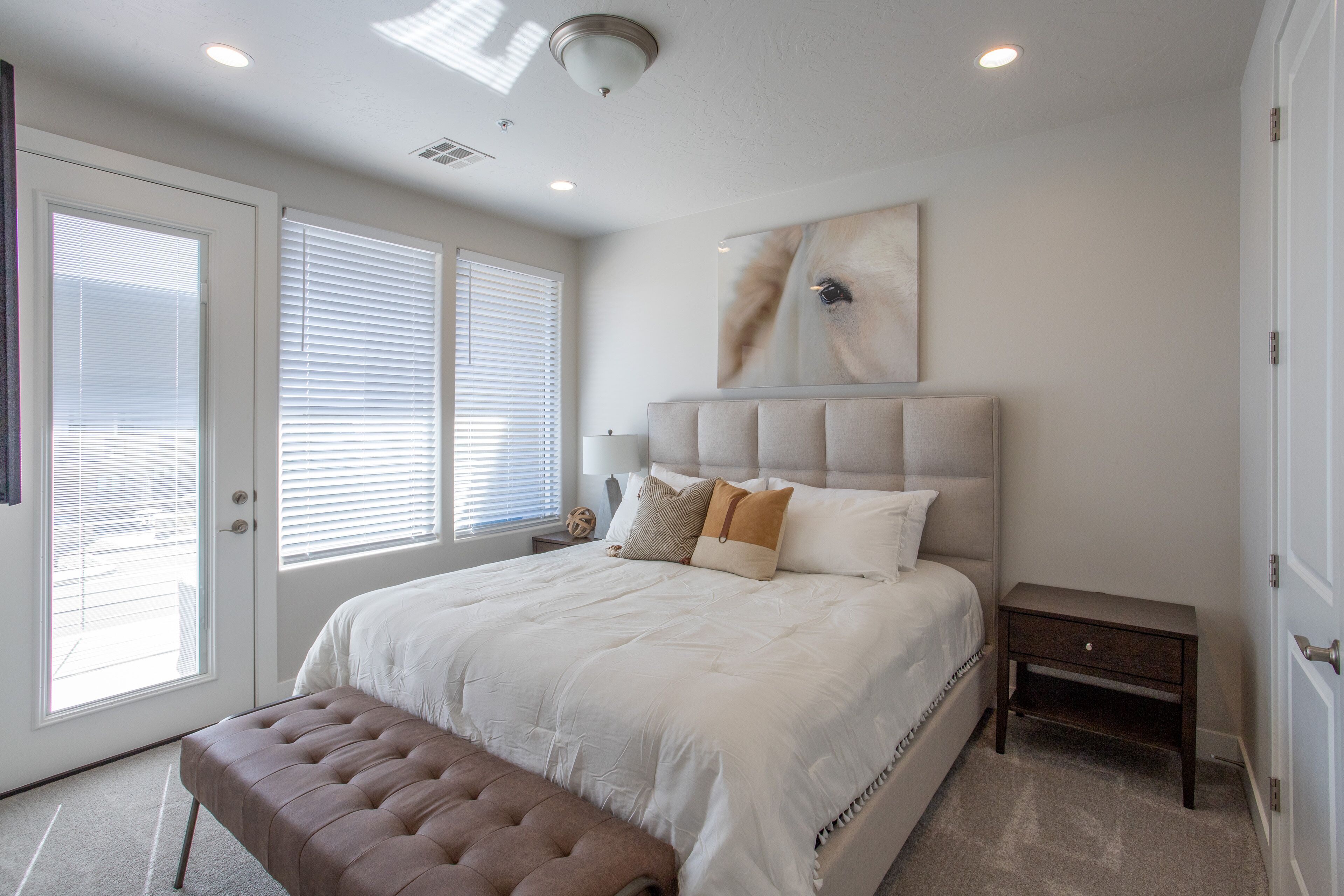A bedroom with a large bed, a bench, a nightstand, and a ceiling light.