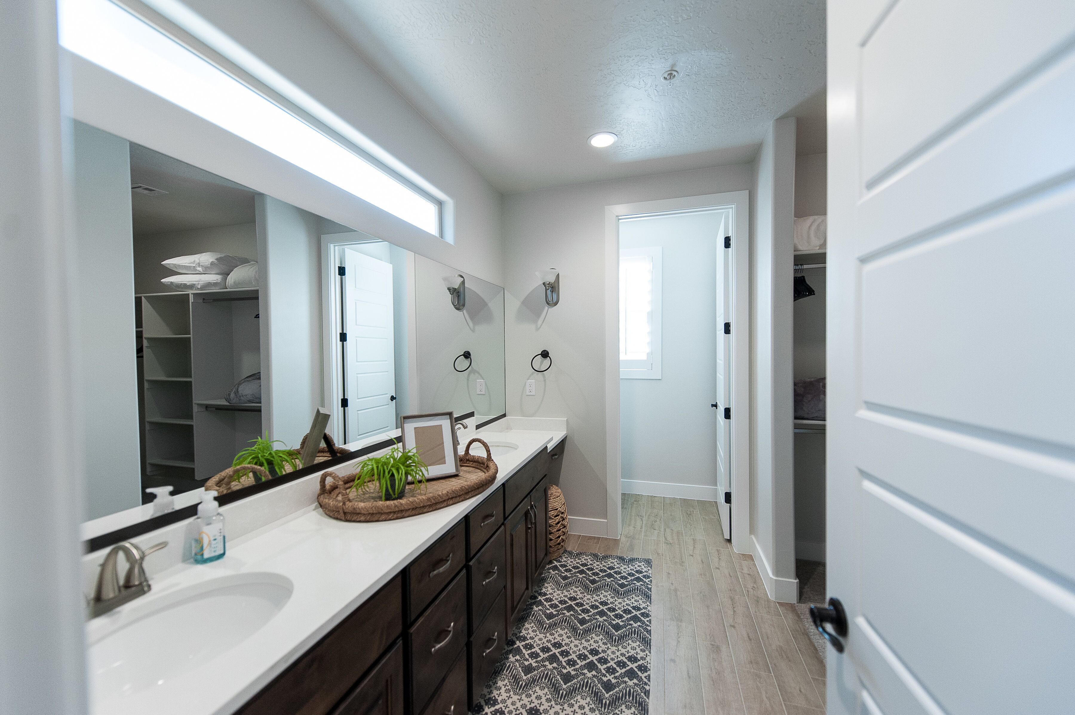 A modern bathroom with a large mirror, double sink, and a walk-in closet.