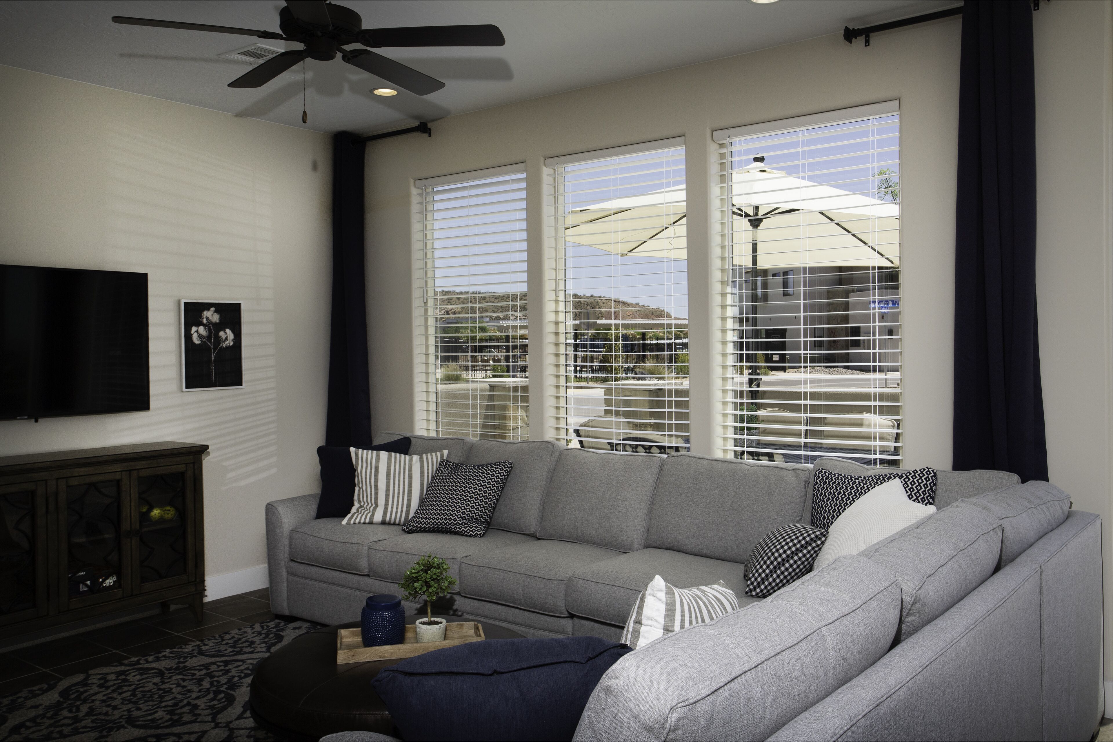 A living room with a gray sofa, a ceiling fan, and a TV mounted on the wall.