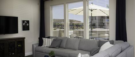 A living room with a gray sofa, a ceiling fan, and a TV mounted on the wall.