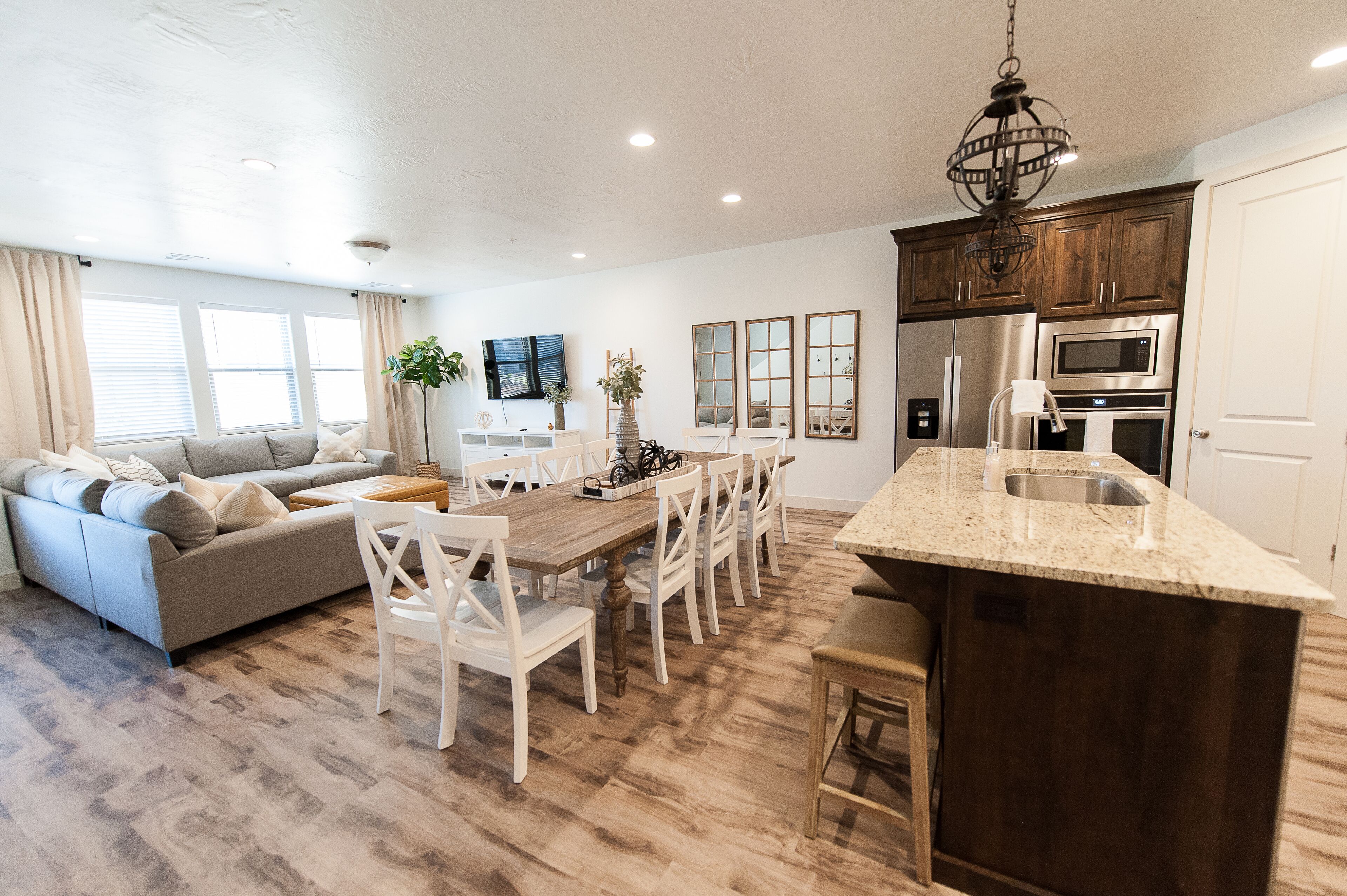 A modern kitchen with a central island, wooden cabinets, stainless steel appliances, and a dining area with a wooden table and white chairs.