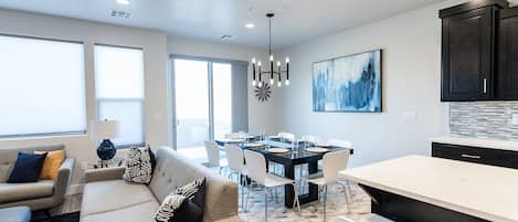A modern kitchen with a dining area, large windows, and a chandelier.