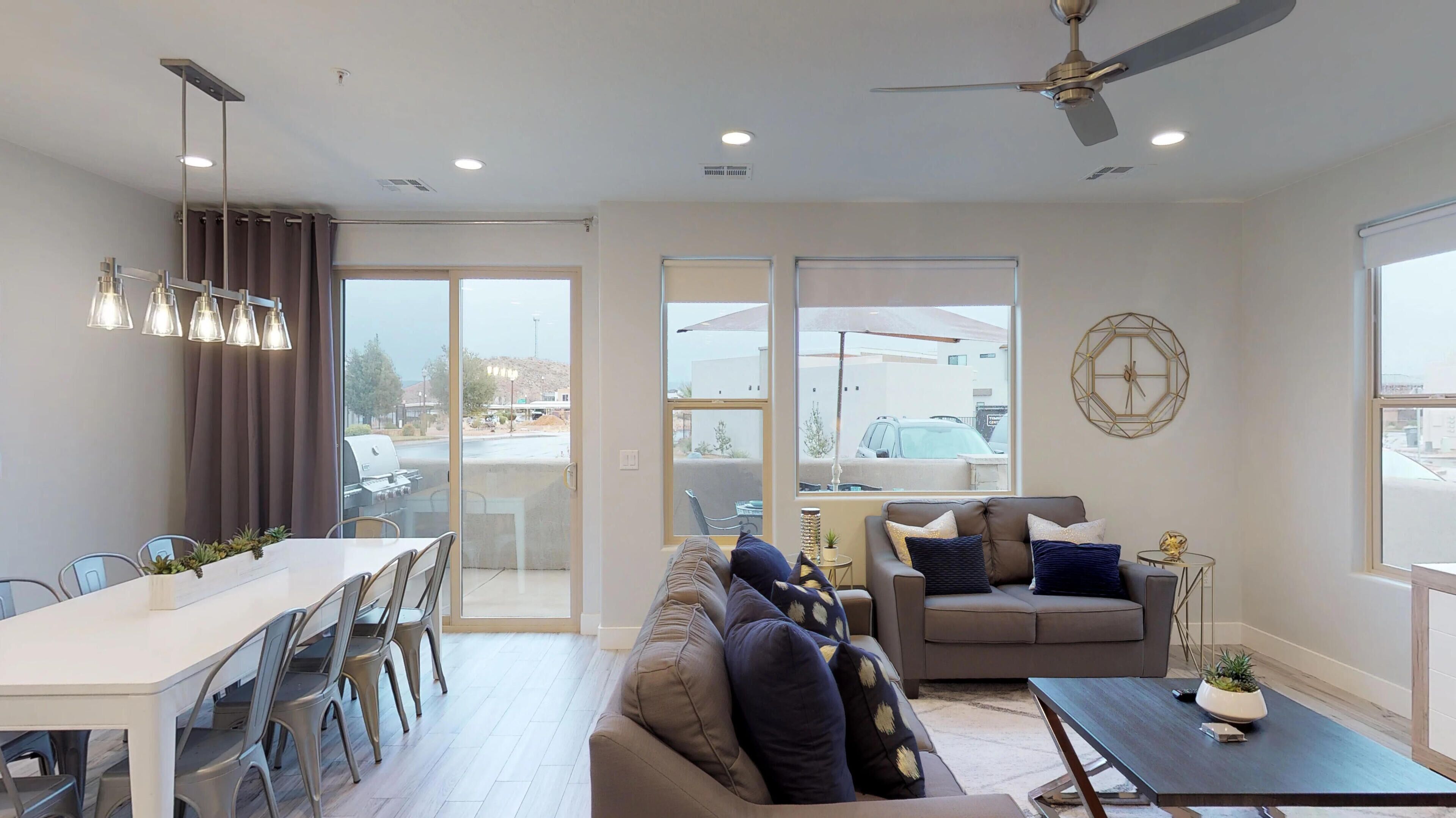 A modern living room with a dining area, large windows, and a ceiling fan.