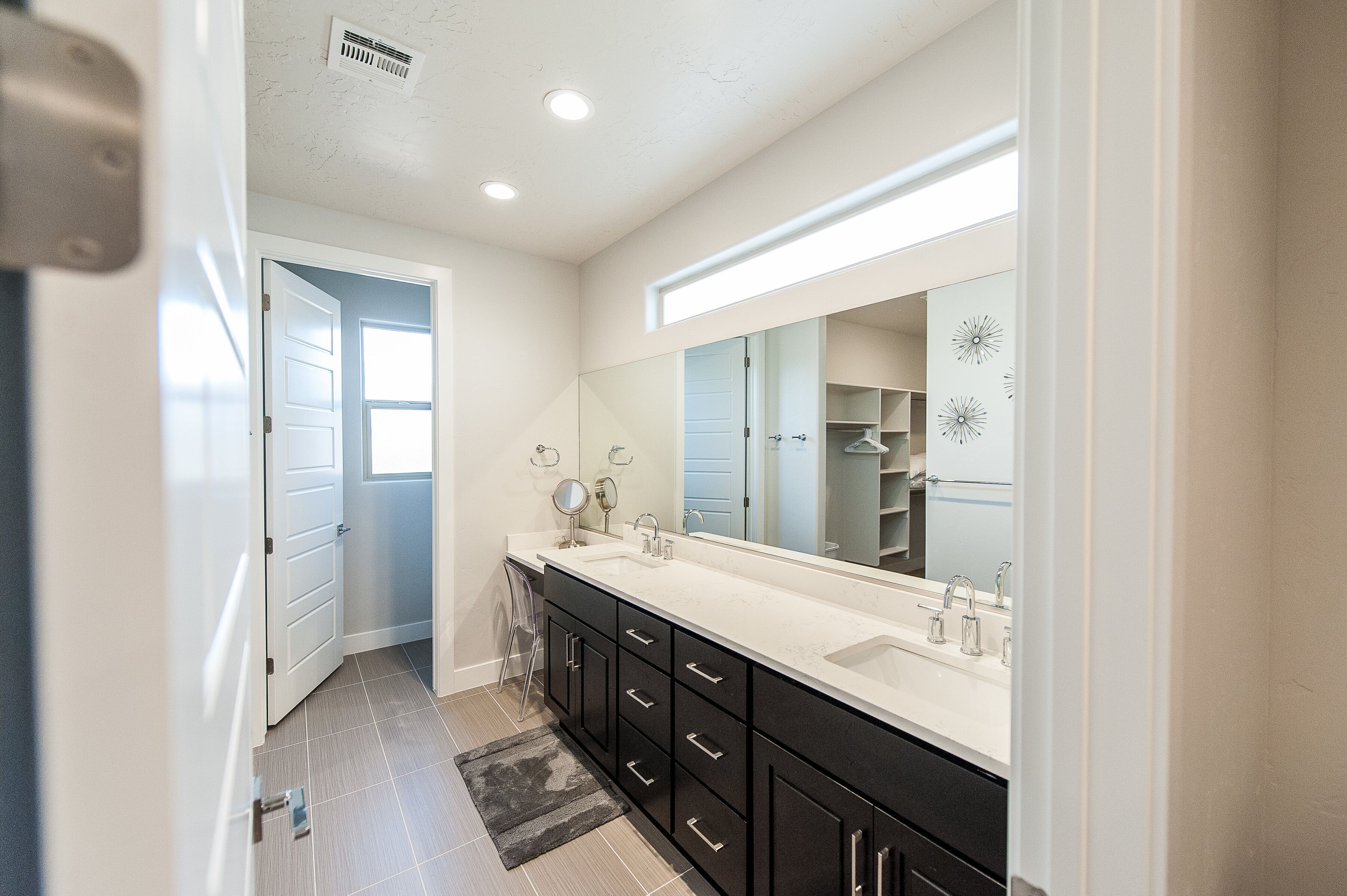 A modern bathroom with a large mirror, two sinks, and a walk-in closet.