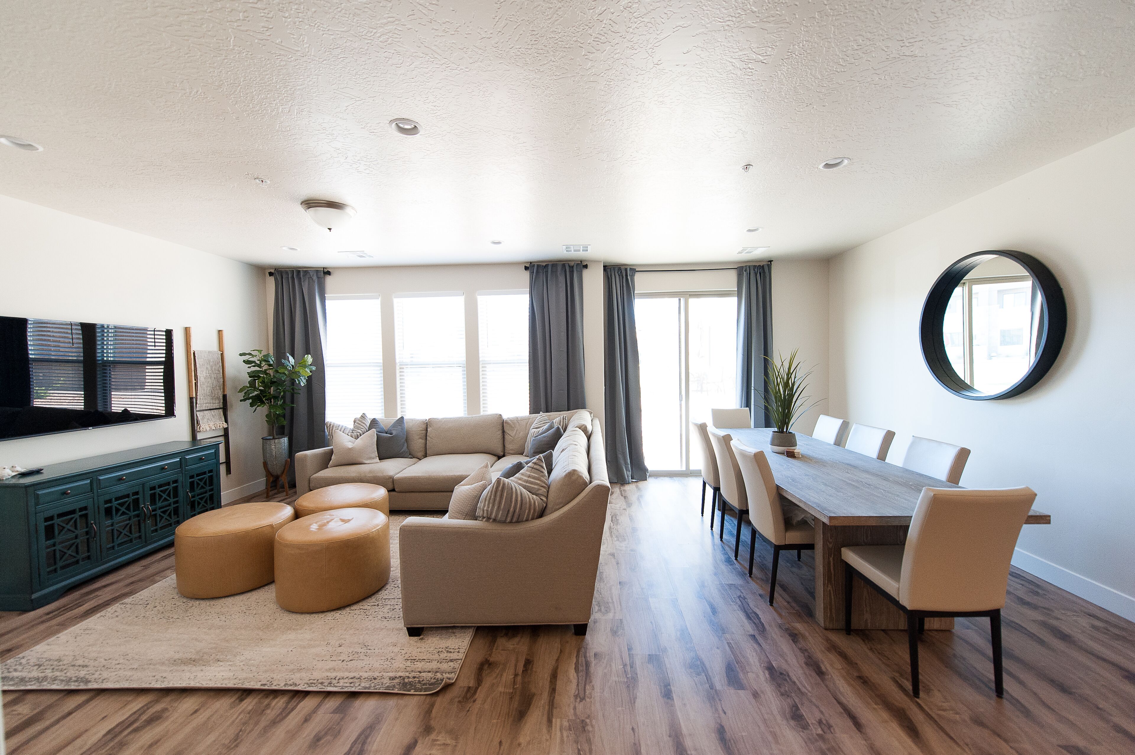 Un salon spacieux avec un grand canapé, des poufs, une table à manger avec des chaises et un téléviseur posé sur un meuble.